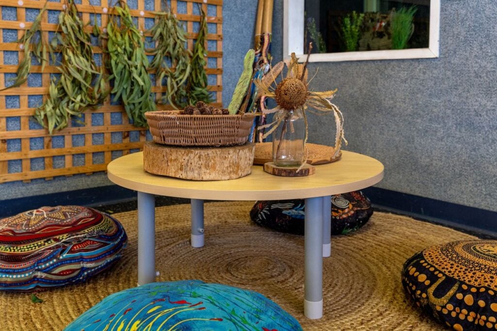 Sitting area with cushions and wooden table in the middle, the table decorated with dried plant.