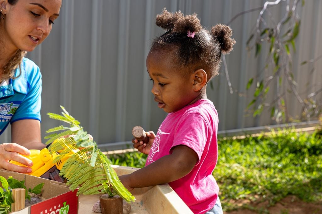 Teacher and Child in pink t-shirt in the garden area, exploring plants.