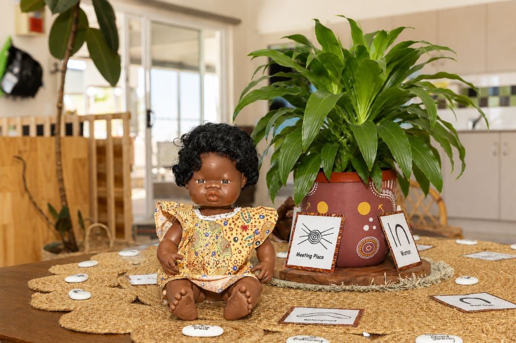 Aboriginal doll in a traditional print dress displayed with Indigenous Australian symbol cards and a decorated plant pot in a childcare learning area